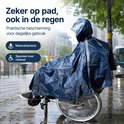 Vrouw in rolstoel met donkerblauwe regenponcho, capuchon, reflecterende strepen. Buitensetting met regen.