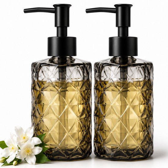 Twee glazen zeepdispensers met honingkleurige vloeistof en witte bloemen.