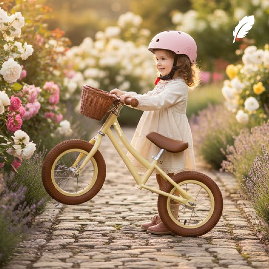 Meisje met roze helm en jurk zit op gele loopfiets met bloemenmandje, fietsend in tuin.