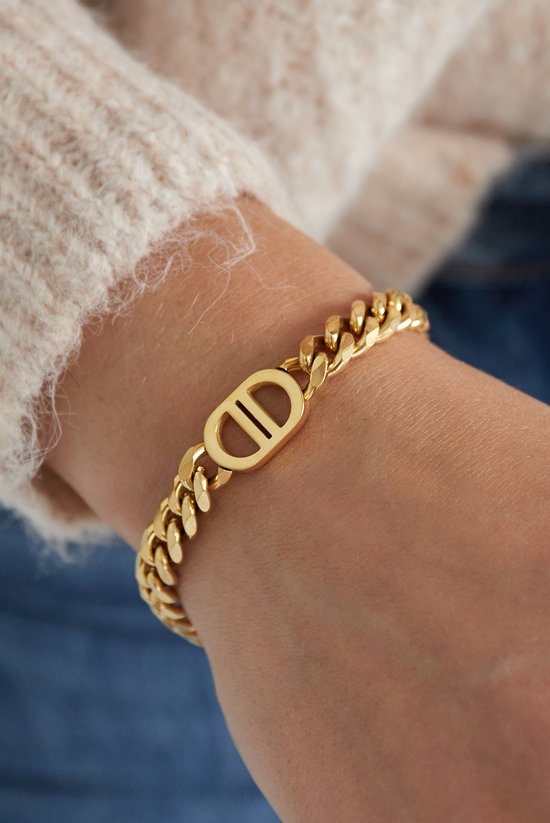Gouden armband met schakels en CD-logo op een pols.