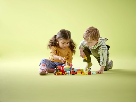 Twee kinderen spelen met een LEGO DUPLO Mickey & Minnie verjaardagstrein op een lichtgroene achtergrond.