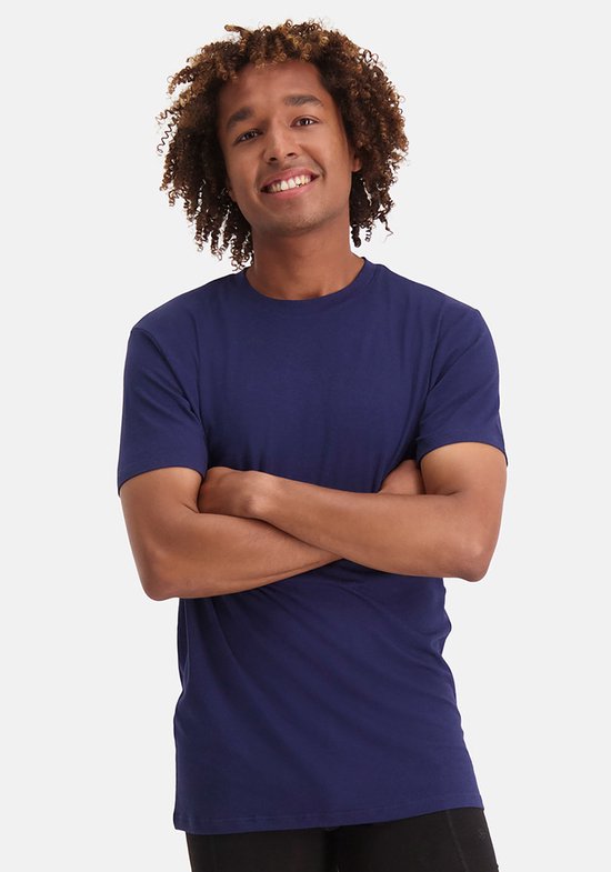 Man met gekruiste armen draagt een marineblauwe T-shirt met ronde hals.