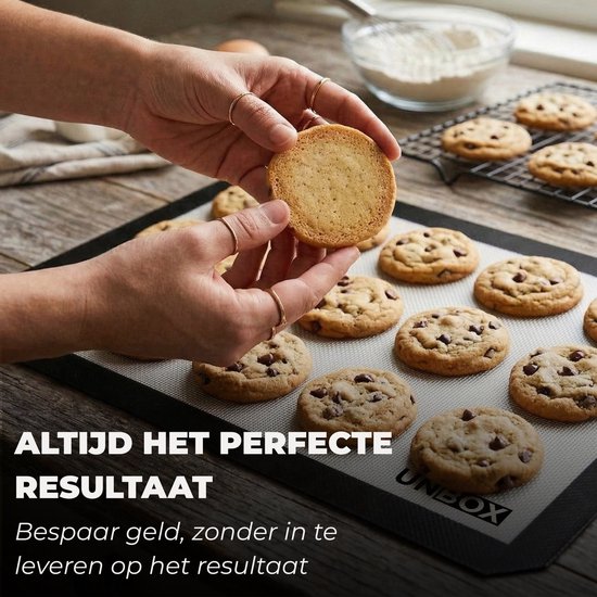 Hand pakt een versgebakken, goudbruine koekje van een beige UNBOX bakmat vol chocoladekoekjes.