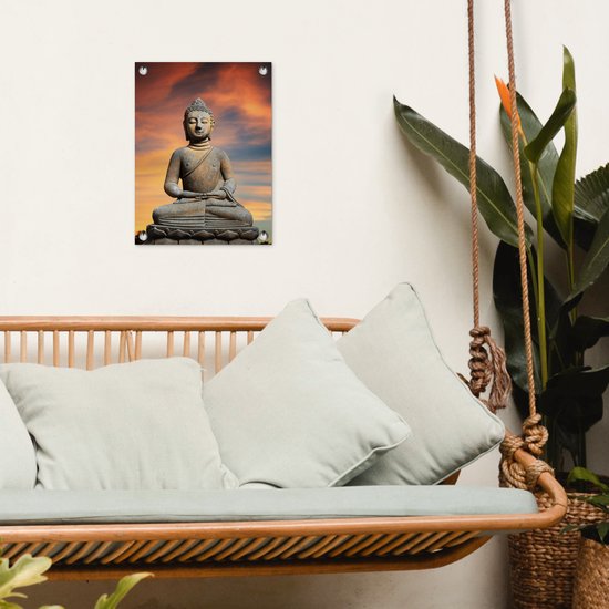 Bouddha en pierre sur fleur de lotus sur fond de coucher de soleil orange, suspendu à un mur blanc à côté d'un hamac.