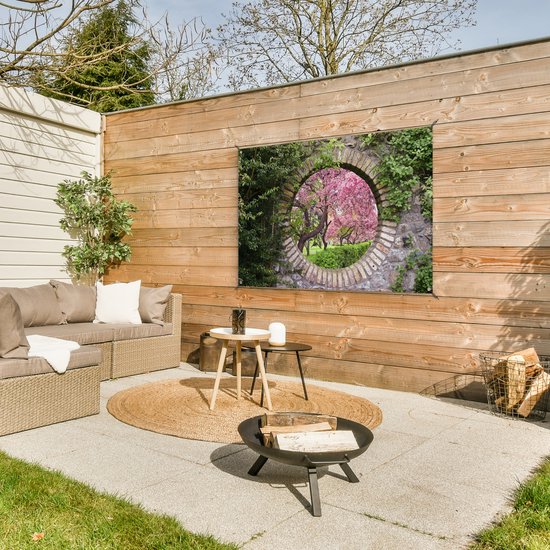 Vue d'un cerisier sakura en fleurs à travers un cercle de pierre. Accroché à une clôture en bois au-dessus d'un salon de jardin.