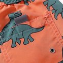 Detail van oranje zwembroek met groene dino print, grijze label en metalen oogje in de zak.