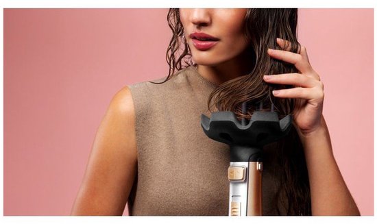 Vrouw met nat haar, hand op haar haar, dichtbij een diffusor-accessoire van een gouden stylingborstel.