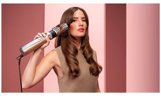 Vrouw met lang bruin haar stylet haar met een gouden en zilveren stylingborstel.