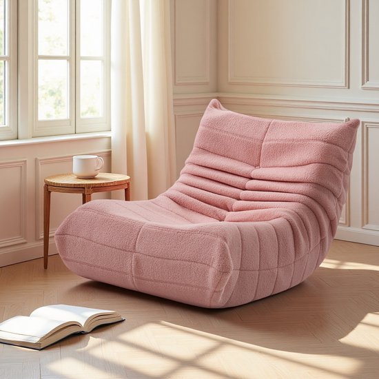 Roze relaxfauteuil met teddy stof in een woonkamer met een raam en houten vloer. De stoel heeft een gerimpelde rugleuning en horizontale naden.