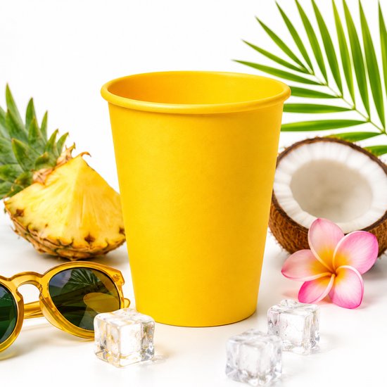 Gele kartonnen beker omringd door ananas, kokosnoot, bloem, zonnebril en ijsblokjes.