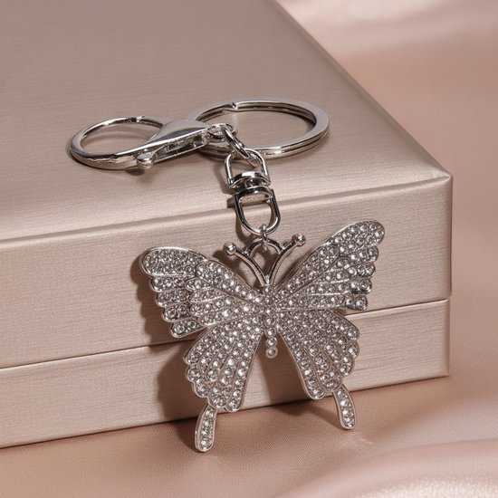Zilverkleurige sleutelhanger met een vlinderbedel vol glinsterende steentjes op een lichtbruine geschenkdoos.