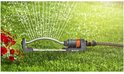 Zwenksproeier met oranje connector en grijze basis op gras, waterstralen spuiten.