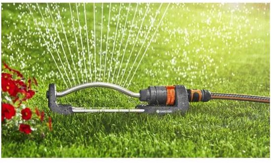 Zwenksproeier met oranje connector en grijze basis op gras, waterstralen spuiten.