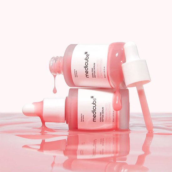 Twee Medicube PDRN Pink Peptide Serum flesjes. Roze serum druipt uit de flesjes en spettert op een roze ondergrond.