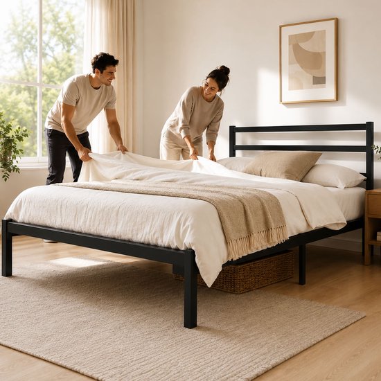 Man en vrouw maken een bed op met een zwart metalen bedframe, in een lichte slaapkamer.