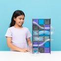 Een meisje met een paarse jurk kijkt naar een hoge Connetix knikkerbaan opgebouwd uit paarse, blauwe en grijze magneetblokken.