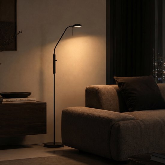 Zwarte staande leeslamp met flexibele nek en verstelbare kop, verlicht een deel van een woonkamer.