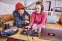 Jong koppel dat aan een tafel met een DJ-controller en laptop zit, met koptelefoons op.