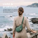 Vrouw met een groene half-moon tas, schoudertas op de rug, aan zee. Licht en praktisch.