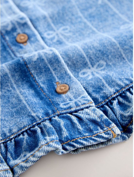Detail van een blauw denim gilet met strikprint, knopen en ruches.