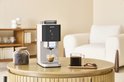 Witte Krups Coffee Crush koffiezetapparaat in een woonkamer setting, met koffiebonen en een kopje koffie ernaast.