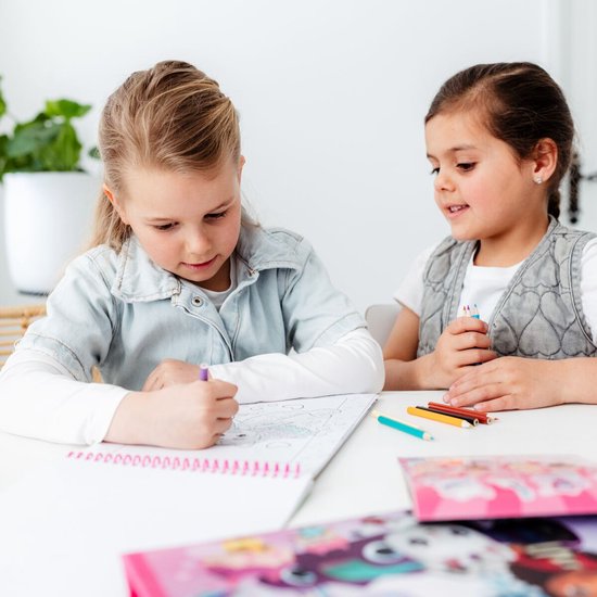 Twee meisjes zitten aan tafel. Eén kleurt in een boek, de ander kijkt toe. Er liggen kleurpotloden.