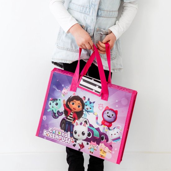Kind met lichte spijkerjas draagt een roze tas met Gabby's Poppenhuis personages, waaronder Gabby en haar katten.