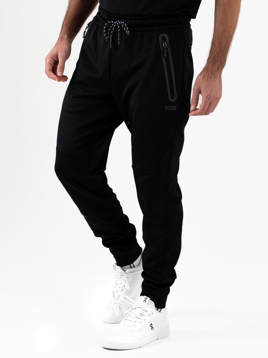 Man draagt zwarte Sjeng Sport trainingsbroek met witte sportschoenen.