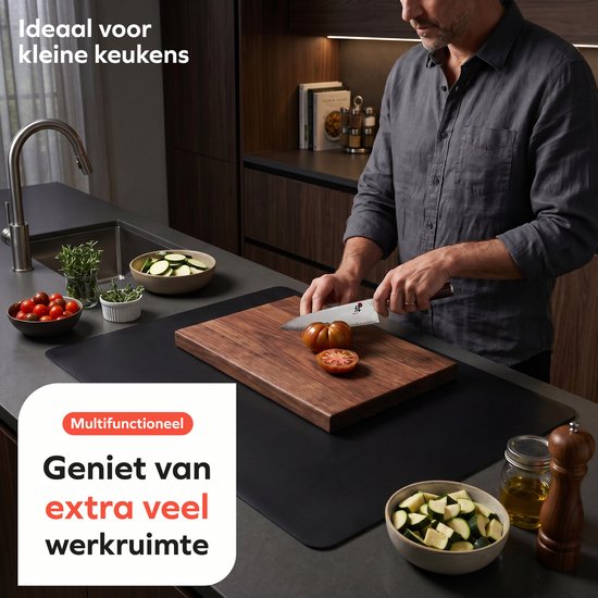 Een man snijdt tomaten op een houten snijplank, die op een zwarte mat ligt. Ideaal voor kleine keukens.