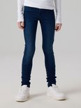 Model draagt een donkerblauwe skinny jeans met witte sneakers.