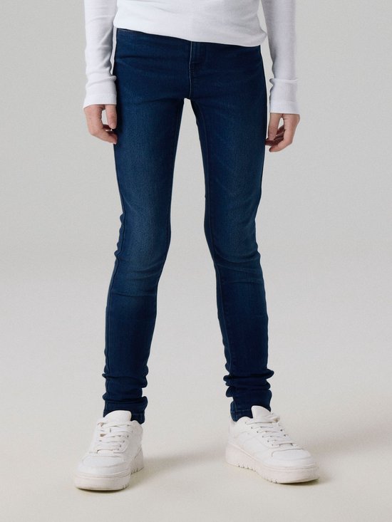 Model draagt een donkerblauwe skinny jeans met witte sneakers.