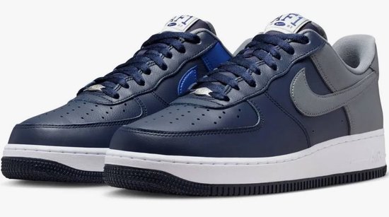 Donkerblauwe Nike Air Force 1 sneakers met grijze en kobaltblauwe panelen. Witte zolen en perforaties op de neus.