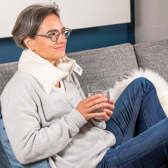 Vrouw met beige nek warmtekussen drinkt glas.