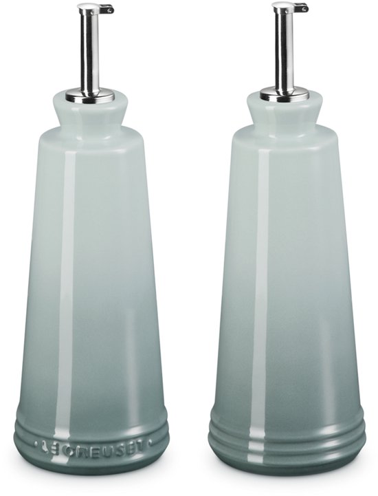 Twee Le Creuset olieflesjes in 'Sea Salt' groen, met zilverkleurige schenktuiten, op zwarte achtergrond.
