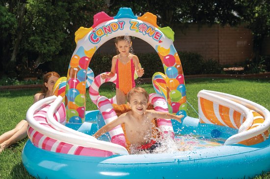 Kinderen spelen in het 'Candy Zone' speelbad met glijbaan, spetterend water onder de snoepboog.
