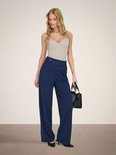 Model draagt donkerblauwe wijde broek met beige top en zwarte tas.