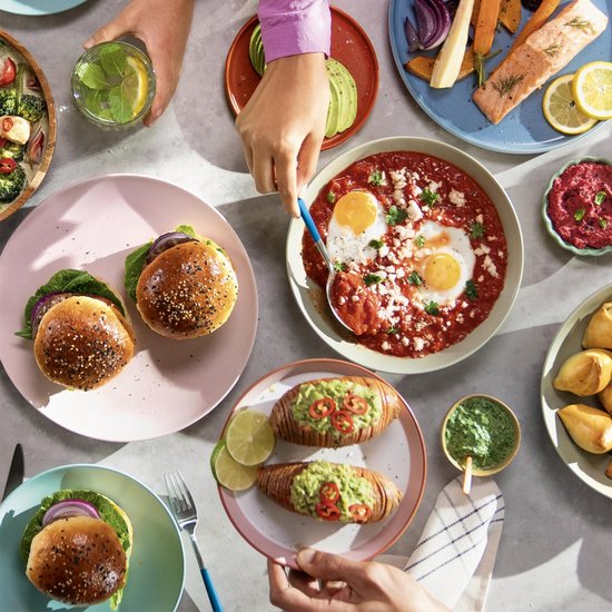 Bovenaanzicht van een tafel vol eten, waaronder burgers, zalm, gepofte aardappelen, salades en een drankje met munt.