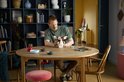 Een man met rood haar, zittend aan een ronde tafel, houdt een LEGO Ideas Gizmo figuur vast. De figuur is gemaakt van bruine en witte blokjes en heeft grote oren.