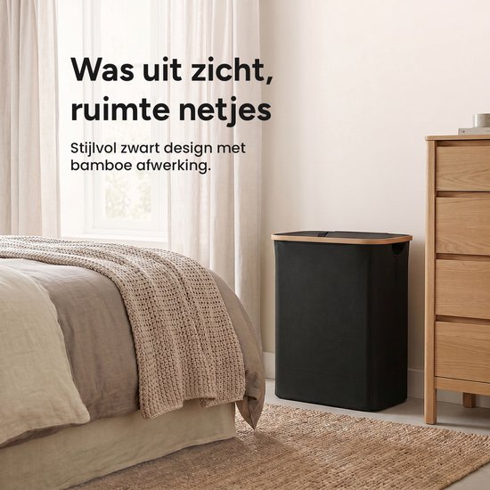Een zwarte, rechthoekige wasmand met bamboehouten afwerking staat naast een houten ladekast in een slaapkamer met een bed en gordijnen.