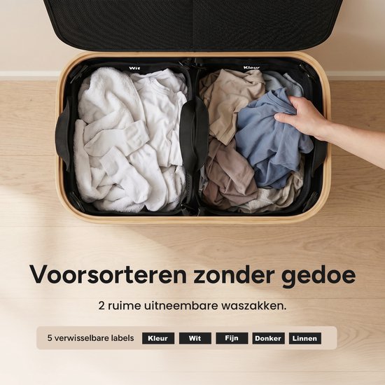 Bovenaanzicht van een open zwarte wasmand met bamboehouten frame, met 2 uitneembare waszakken. Eén zak bevat witte handdoeken, de andere gekleurd wasgoed.