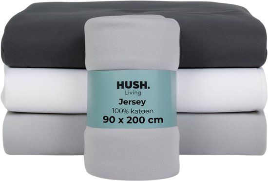 Draps-housses empilés en anthracite, blanc et gris clair. Un drap-housse en jersey gris est enroulé et attaché avec une bande.