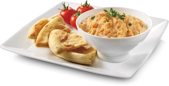 Een witte schaal met een oranje dip, besprenkeld met kruiden, geserveerd met platbrood en cherrytomaten.