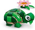 Een groene legoschildpad met een bolle schaal, grote ogen en een roze bloem met groene blaadjes ernaast.