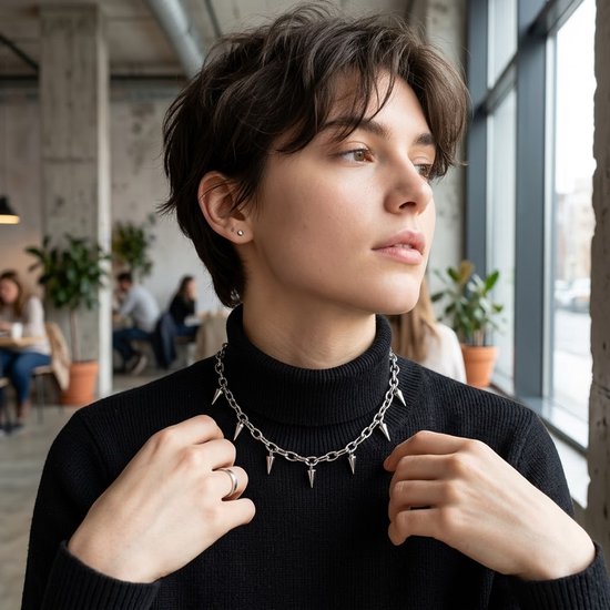 Model met kort bruin haar draagt een zilverkleurige schakelketting choker met puntige spikes en een zwarte coltrui.