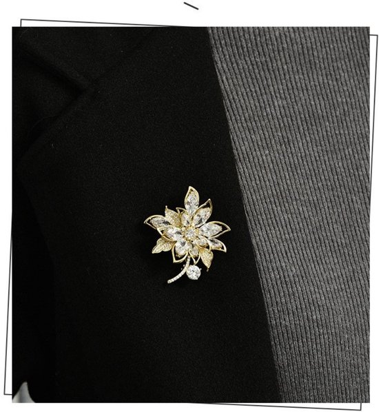Gouden bloemenbroche met heldere stenen op een zwart jasje.