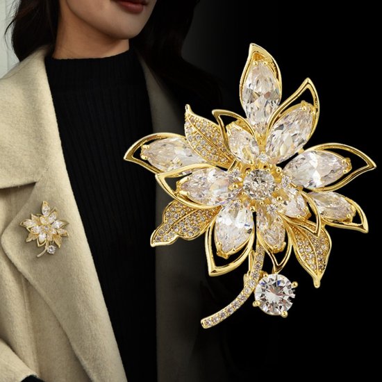 Gouden bloemenbroche met heldere stenen, gedragen op een beige jasje.