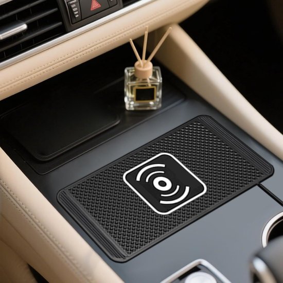 Een zwart, gestructureerd draadloos oplaadpad met een wit Qi-logo in het midden, geplaatst in een beige auto-interieur met een kleine glazen diffuser.