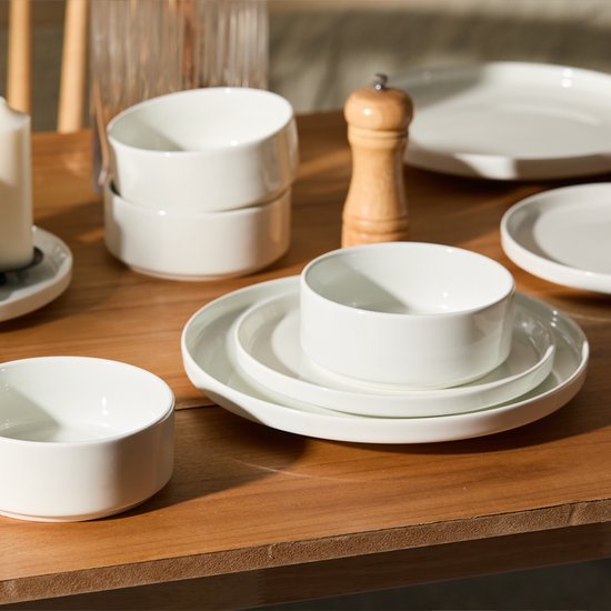 Witte borden en kommen op een houten tafel, naast een kaars en pepermolen.