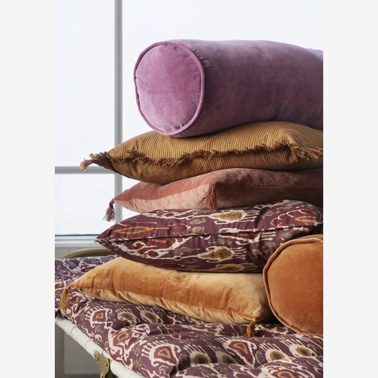 Stapel kussens in verschillende kleuren: paars, oranje, roze en met paisley-print. Een langwerpig paars fluwelen kussen bovenop.