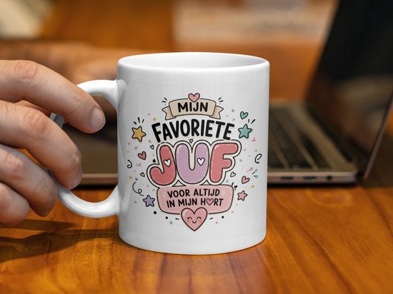 Witte mok met de tekst "MIJN FAVORIETE JUF VOOR ALTIJD IN MIJN HORT" in kleurrijke letters, versierd met hartjes en sterren. Hand houdt de mok vast.